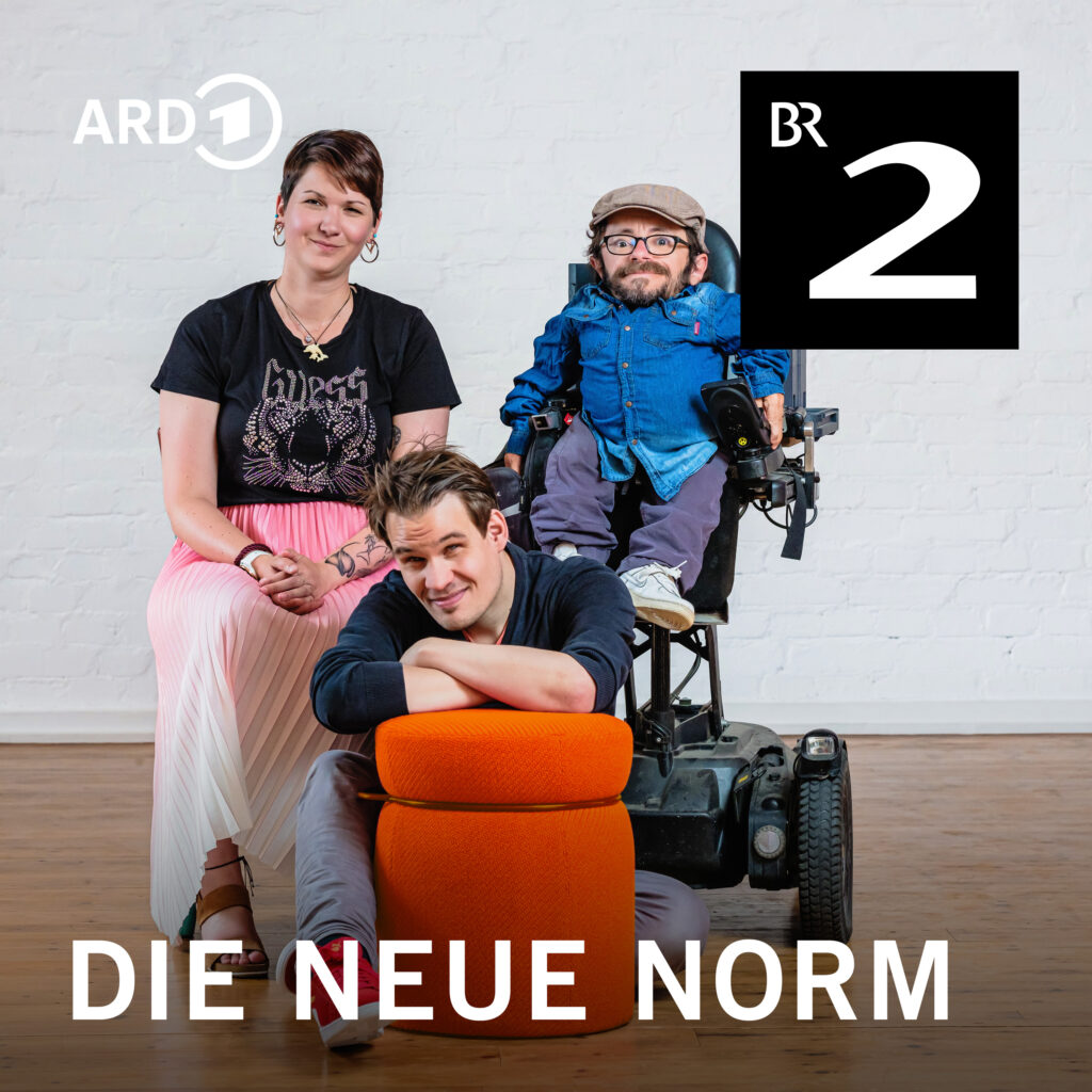 Podcast Logo von Die Neue Norm. Karina Sturm sitzt auf einem Stuhl. Sie hat kurze dunkle Haare, trägt ein schwarzes t-Shirt und einen pink-weißen Rock. Neben ihr sitzt Raúl Krauthausen in einem Elektrorollstuhl. Er trägt eine graue Mütze und ein blaues Hemd. Vor ihnen sitzt Jonas Karpa auf dem Boden. Er trägt einen schwarzen Pullover und stützt sich auf einem orangenen Sitzhocker ab. Alle schauen in die Kamera.